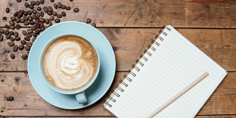 arial photo of a full cup of coffee and a notepad on a wooden table